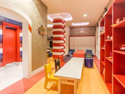 Kolorowy pokój zabaw dla dzieci z żółtymi krzesłami, długim stołem i czerwonymi półkami w hotelu.