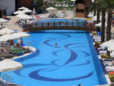 Duży niebieski basen hotelowy z mozaikowym wzorem, leżakami i białymi parasolami wokół.