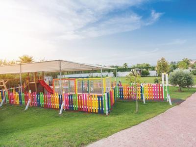 Kolorowy plac zabaw dla dzieci ze zjeżdżalnią, otoczony trawą i ścieżką pod błękitnym niebem.