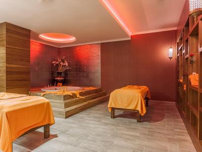 Une salle de spa confortable avec deux tables de massage et un éclairage orange chaud.