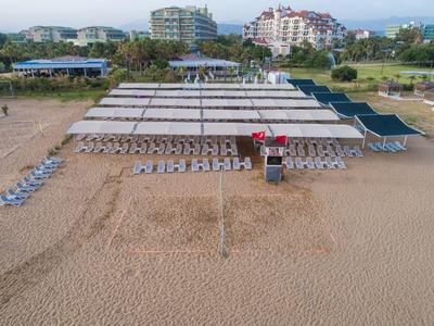 Area della spiaggia ben organizzata con lettini, tende da sole e hotel sullo sfondo.