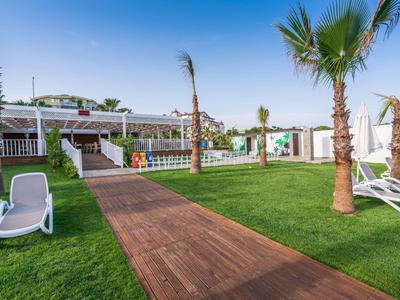 Giardino dell'hotel con lettini, percorso in legno e piscina circondata da palme sotto un cielo azzurro.