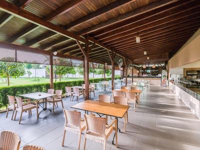 Terrazza esterna aperta dell'hotel con tetto in legno, tavoli e sedie lungo il bar.