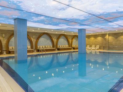 Grande piscina coperta con piastrelle blu e soffitto a tema nuvole in un hotel.
