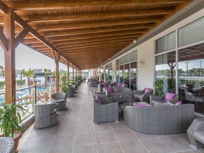 Terrazza coperta dell'hotel con aree salotto e vista su piscina e giardino sullo sfondo.