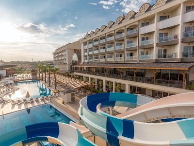 Hotel moderno con piscina all'aperto, scivoli d'acqua e lettini sotto un cielo azzurro.