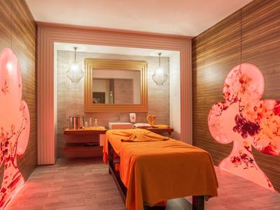 Accogliente sala massaggi con due lettini, illuminazione calda e decorazioni murali.