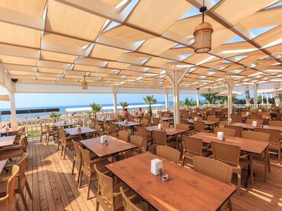 Duży zadaszony taras z drewnianymi stołami i widokiem na morze w słoneczny dzień.