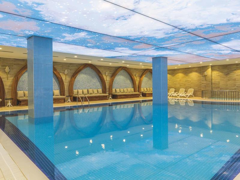 Basen kryty z niebieską wodą, oświetleniem sufitowym i oknami łukowymi w hotelu