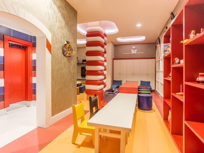 Kolorowy pokój zabaw dla dzieci z żółtymi krzesłami, długim stołem i czerwonymi półkami w hotelu.