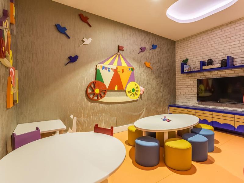 Kolorowy pokój zabaw dla dzieci z okrągłymi stołami, kolorowymi taboretami i dekoracją ścienną cyrku.