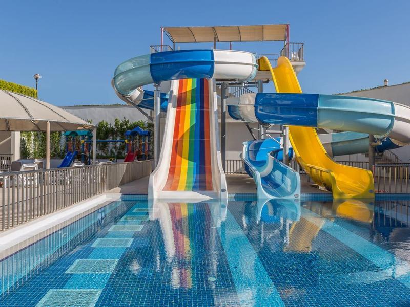 Kolorowy kompleks zjeżdżalni wodnych z kilkoma zjeżdżalniami obok basenu pod niebieskim niebem.