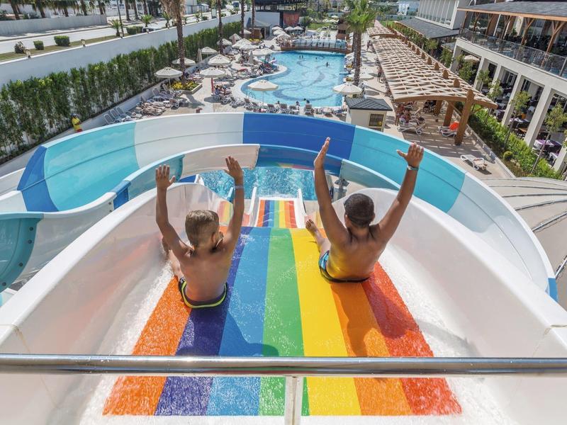 Dwie kobiety zjeżdżają kolorowymi zjeżdżalniami wodnymi do basenu hotelowego.