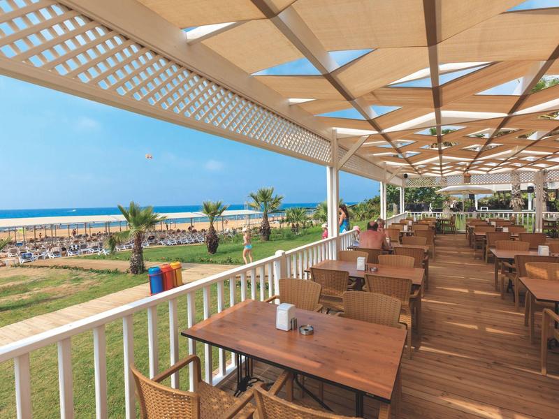 Zadaszony taras zewnętrzny z drewnianymi stołami z widokiem na plażę i morze.