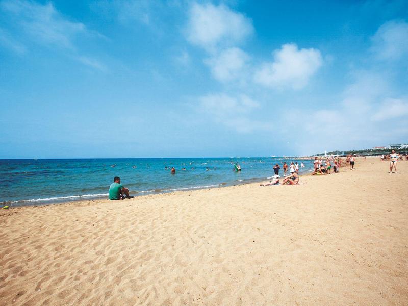 Szeroka piaszczysta plaża z niewielką liczbą ludzi i niebieskim niebem nad morzem.