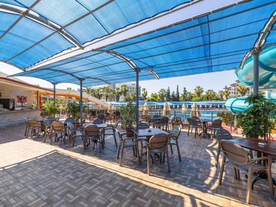 Terraza al aire libre con mesas y sillas bajo techo azul junto a una piscina en un hotel.