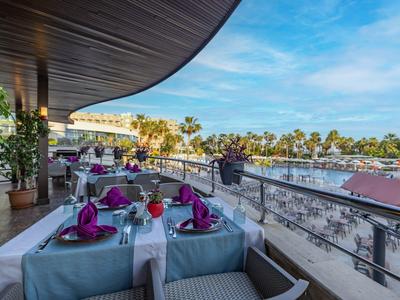Terraza exterior de un hotel con mesas preparadas con vista a la piscina y palmeras.