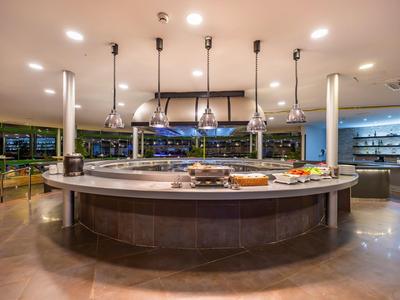 Mostrador circular de buffet en comedor moderno con lámparas colgantes y amplias ventanas.