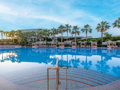 Grande piscina dell'hotel con lettini e palme sotto un cielo azzurro.