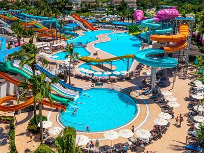 Parco acquatico colorato con più piscine, scivoli d'acqua e lettini circondati da palme.