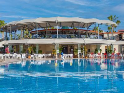 Piscina moderna dell'hotel con tettoia parasole e posti a sedere sotto un cielo soleggiato.
