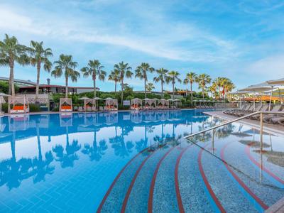 Grande piscina dell'hotel con palme e lettini sotto un cielo azzurro.