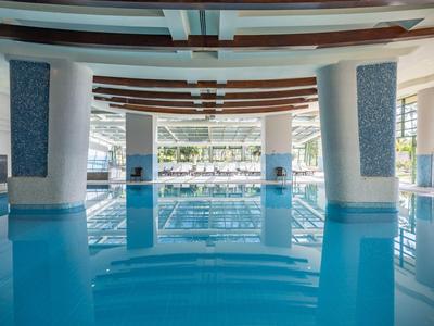 Grande piscina interna con piastrelle blu, colonne bianche e ampie finestre in un hotel di lusso.