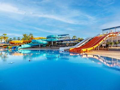 Grande piscina blu con scivoli d'acqua e palme in una giornata di sole.