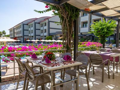 Terrazza esterna di un hotel con tavoli apparecchiati e fiori vivaci lungo la ringhiera.