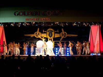 Ballerini si esibiscono sul palco con costumi colorati davanti a uno sfondo di monete d'oro.