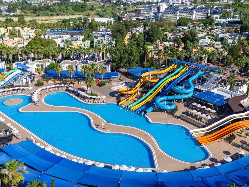 Gran parque acuático con varios toboganes y grandes piscinas, rodeado de árboles y edificios.