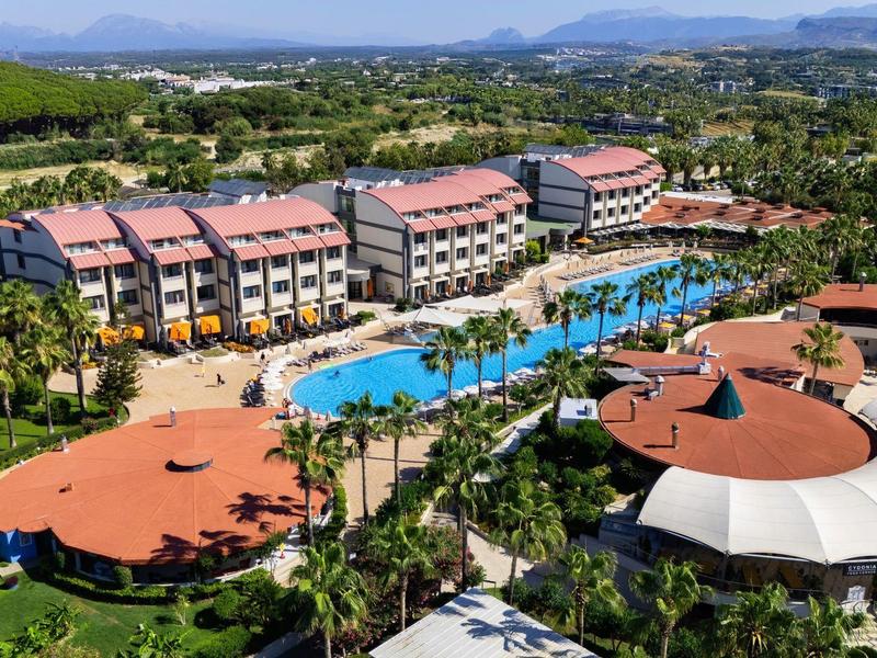 Resort con piscina larga, edificios con techos rojos y áreas verdes, en zona tropical y montañosa.