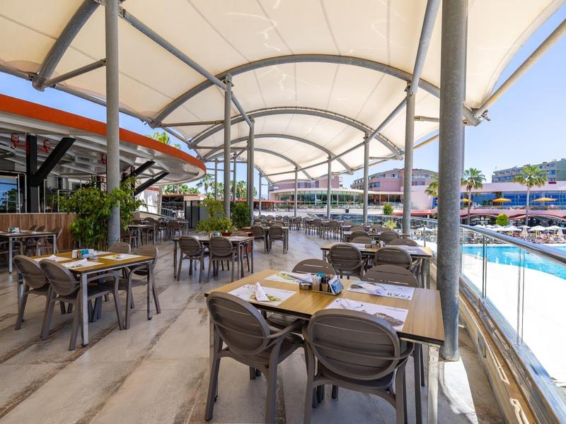 Terraza exterior cubierta con mesas y sillas junto a una piscina en un hotel.