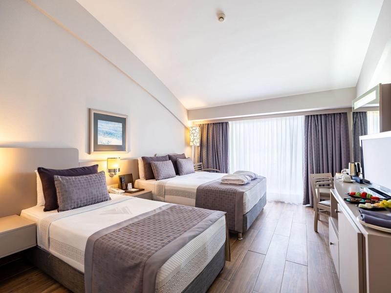 Habitación de hotel con dos camas individuales, decoración moderna y balcón con cortinas.