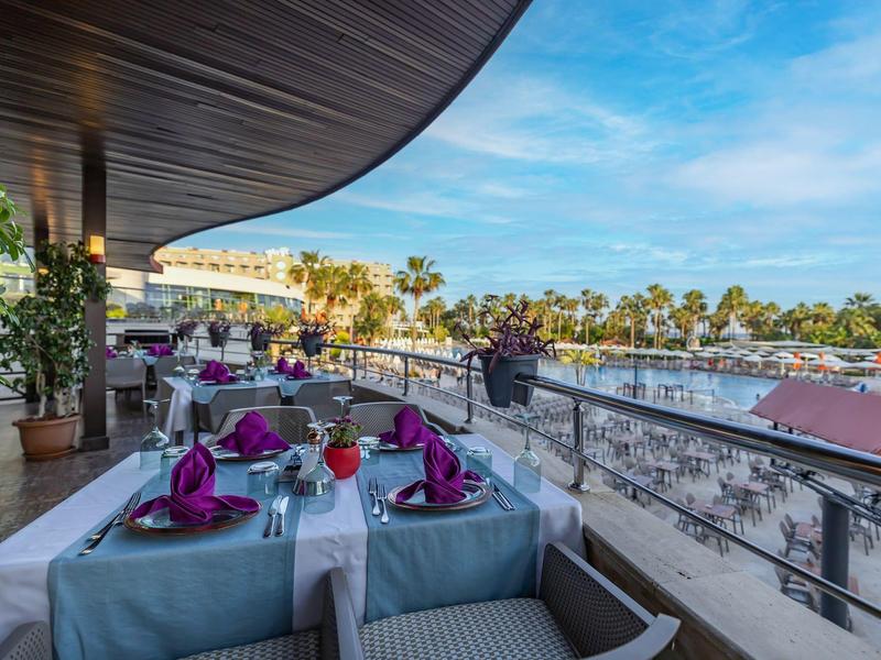 Terraza exterior de un hotel con mesas preparadas con vista a la piscina y palmeras.