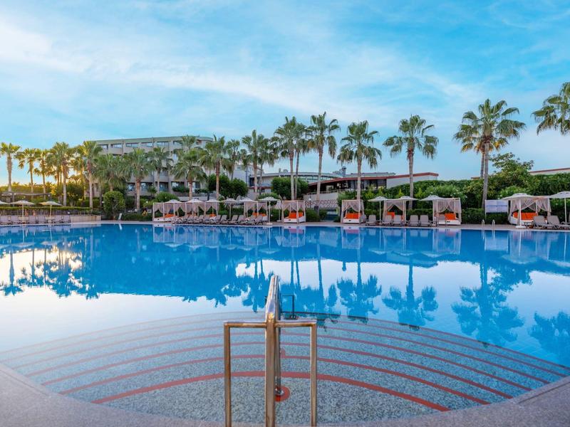 Amplia piscina al aire libre rodeada de palmeras y tumbonas bajo un cielo despejado.