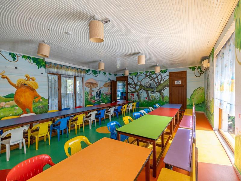 Comedor colorido con mesas largas y sillas de varios colores en un ambiente decorado con murales de naturaleza.