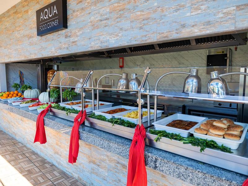 Área de buffet con varios contenedores de comida, cubiertos y decorados con bolsas rojas.