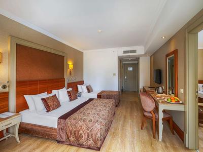 Hotel room with two beds, wooden floor, desk with chair, and warm lighting.