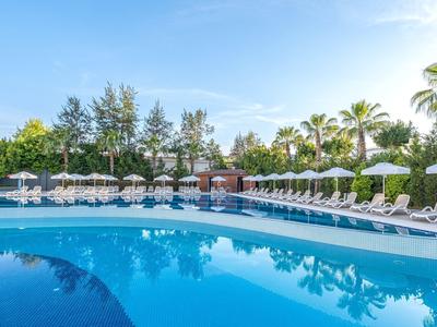 Outdoor pool surrounded by white lounge chairs and umbrellas under a clear blue sky.