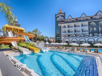 Resort pool with water slides, lounge chairs, and a multi-story hotel building under clear skies.