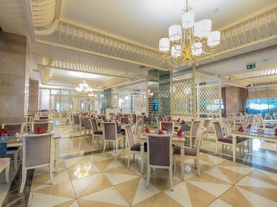 Spacious hotel dining area with elegant chairs, tiled floor, and bright chandeliers.