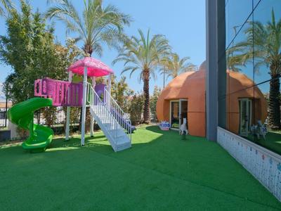 Outdoor kids' playground with slides and curved structure near palm trees on green artificial turf.