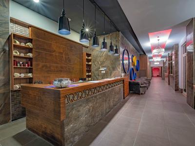 Modern hotel reception area with stone and wood counter, pendant lights, and hallway seating.