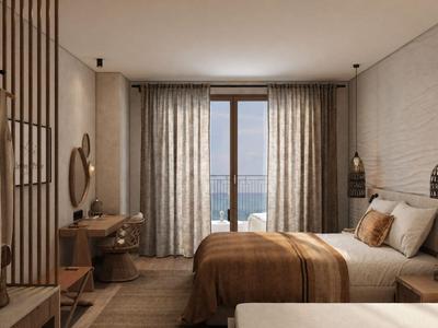 Modern hotel room with double bed, armchair, and balcony overlooking the sea.