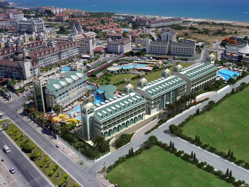 A large hotel complex with multiple pools near the coastline and green fields.