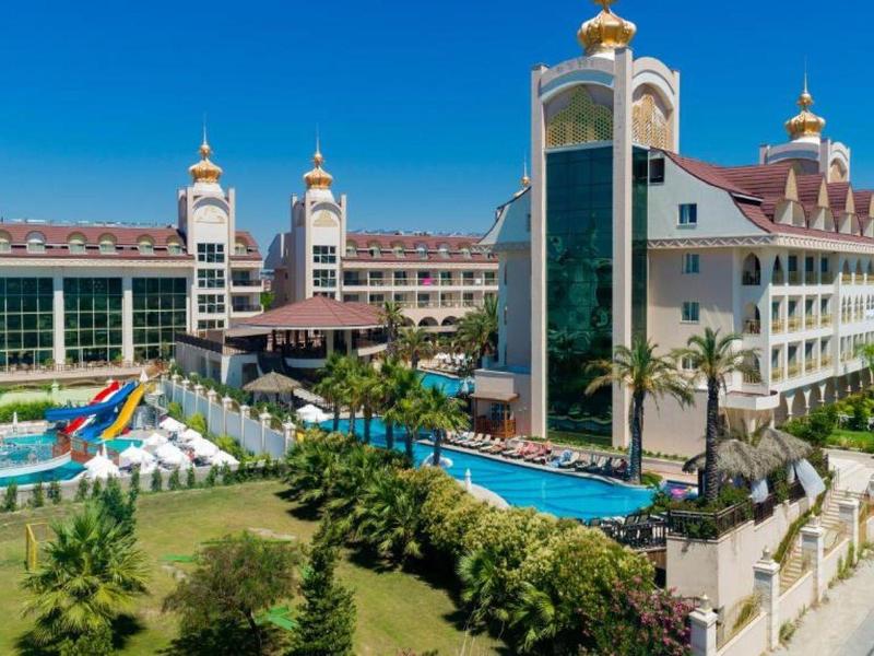 Large luxury hotel with pools, sun umbrellas, water slides, and garden by the sea.
