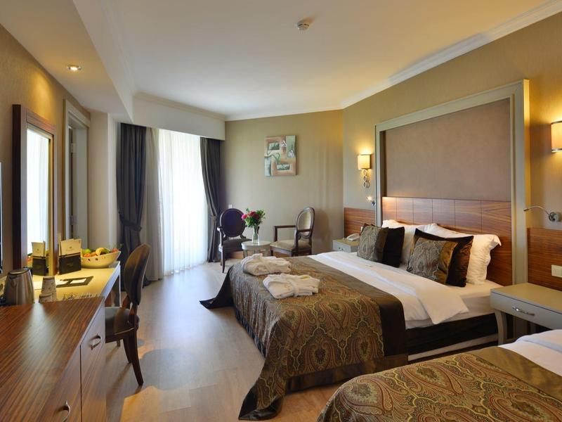 Modern hotel room with two beds, desk, TV, and large window with curtains.