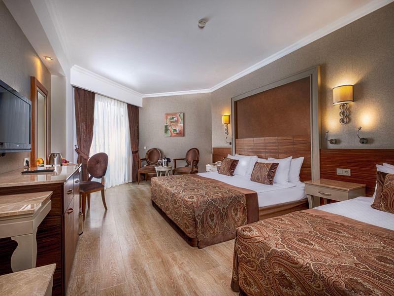 Spacious hotel room with two beds, wooden flooring, chairs, and a flat-screen TV.