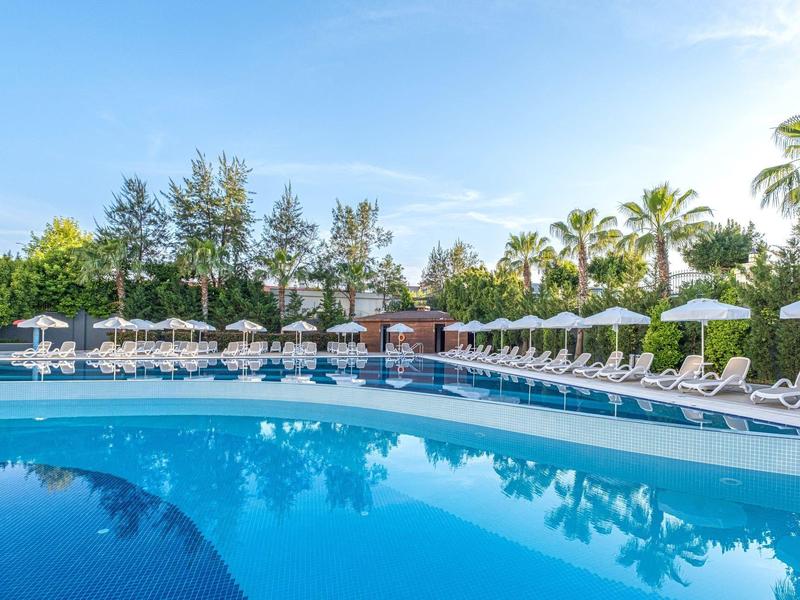 Outdoor pool surrounded by white lounge chairs and umbrellas under a clear blue sky.